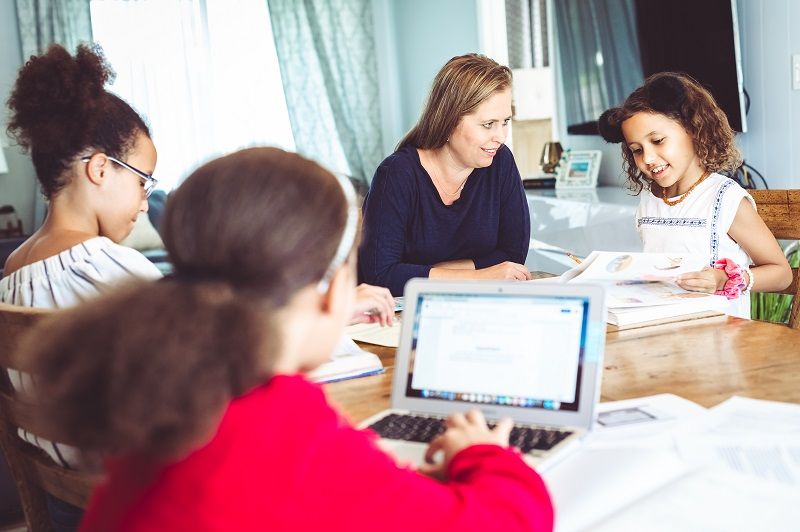 Mother of three supervises her school age daughters at home doing distance learning or schoolwork cm